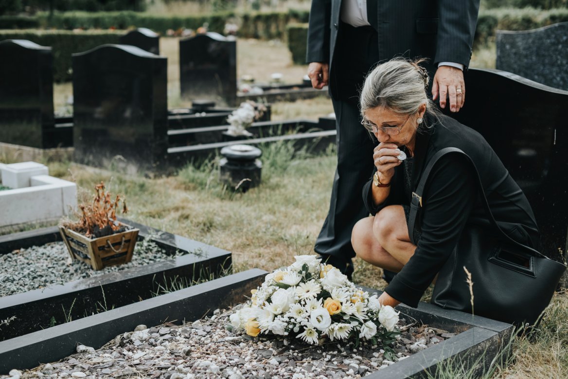 anguished woman dressed in black kneeling at gravesite
